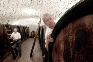 Andreas and Hans between big wooden casks. Hans has one foot on a ladder, Andreas looks out from behind one of the casks.