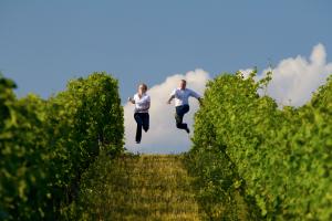 Kathrin and Andreas run downhill between rows of grapevines and jump into the air with stretched-out feet.