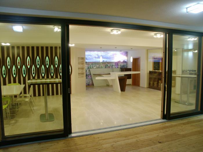 Big Glass sliding door with two open wings. Through that the tasting rom with tables and a bar are visible.