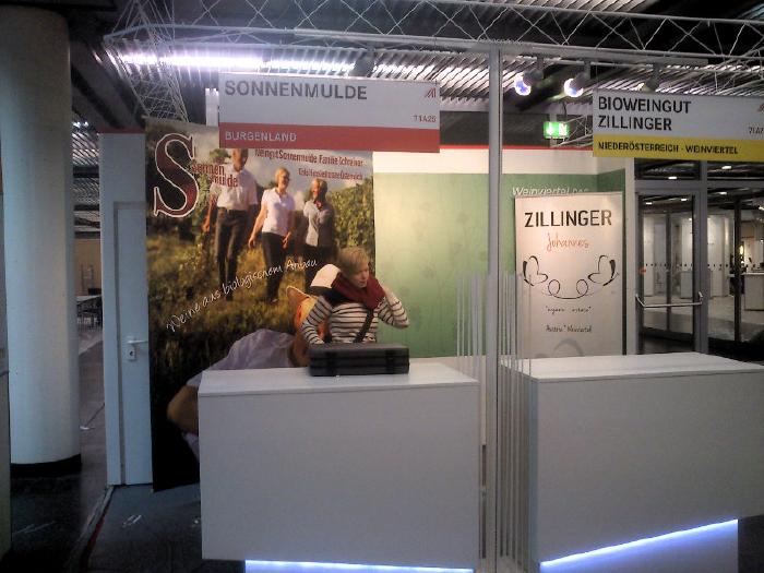 Kathrin at the still undecorated desk of the booth. Above it hangs a board with our name on it, at the back of the wall there is a photo of the family.