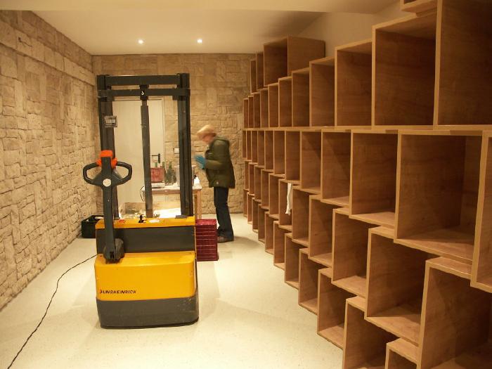 An electric pallet jack in the vinotheque. Behind it Renate at a table sorting bottles