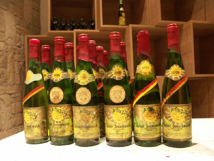 Bottles with old labels on a table in front of the vinotheque's shelves.