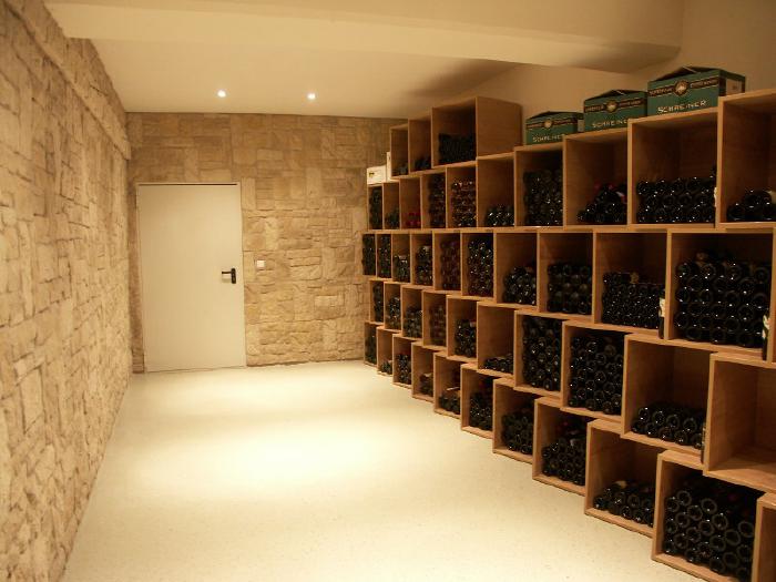 An elongated room with stone walls on the left and at the head end where there is also a door. The right wall is taken up by shelves with compartments for wine bottles.