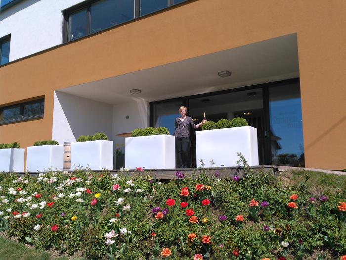 View towards the tasting room's entrance with flowerpots in front of it. Kathrin is waiting with a bottle of Frizzz.