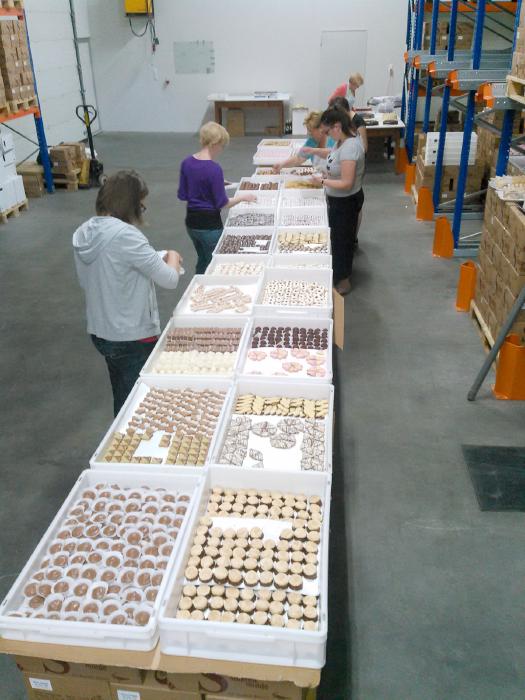 A 10 meter long board, covered with boxes full of cookies from which women fill paper plates and small boxes.