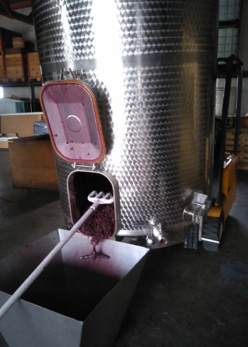 A stainless steel red wine fermentation cask with an open door. Fermented mesh is moved into the press one level below using a funnel and a hole in the floor