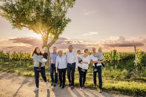 The Schreiner Family with children, parents and grandparents walks towards the camera out from a vineyard with a walnut tree.