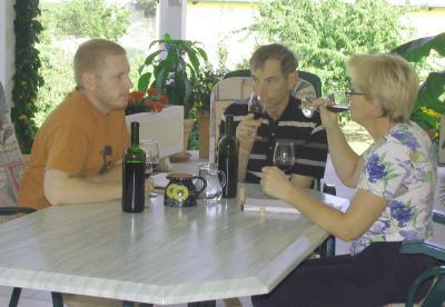 Hans, Renate und Andreas sitzen an einem Terassentisch mit Weinflaschen und Gläsern darauf.