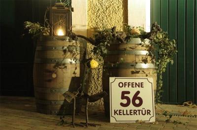 Zwei Barriques mit herbstlichem Laub dekoriert. Auf einem steht eine Laterne mit brennender Kerze. Davor eine Tafel mit dem Hinweis auf die Offene Kellertür Nr. 56.