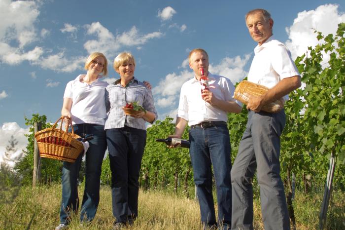 Familie Schreiner steht mit Brot, Wein und Picknickkorb zwischen Rebzeilen im Gras.
