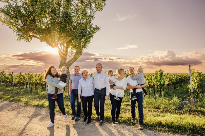 Familie Schreiner steht mit Brot, Wein und Picknickkorb zwischen Rebzeilen im Gras.